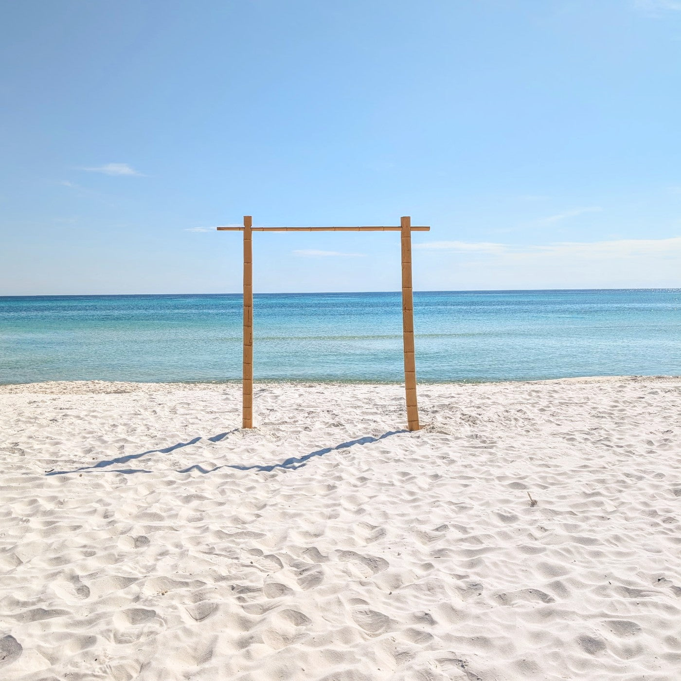 Bamboo wedding arch rental in Panama City beach on the sandy beach with clear blue sky and ocean.