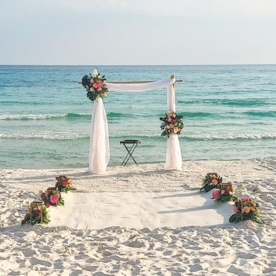 Beach wedding setup with floral arch and decorations in front of the ocean.