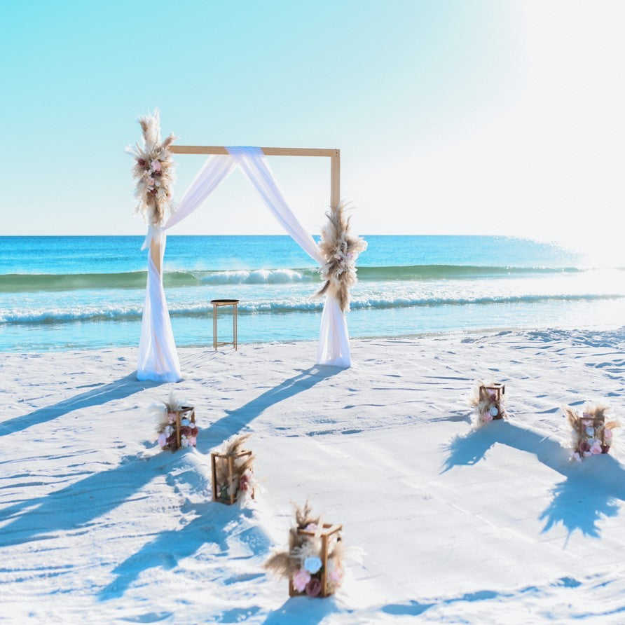 Beach wedding setup with arch and chairs on a sandy beach.