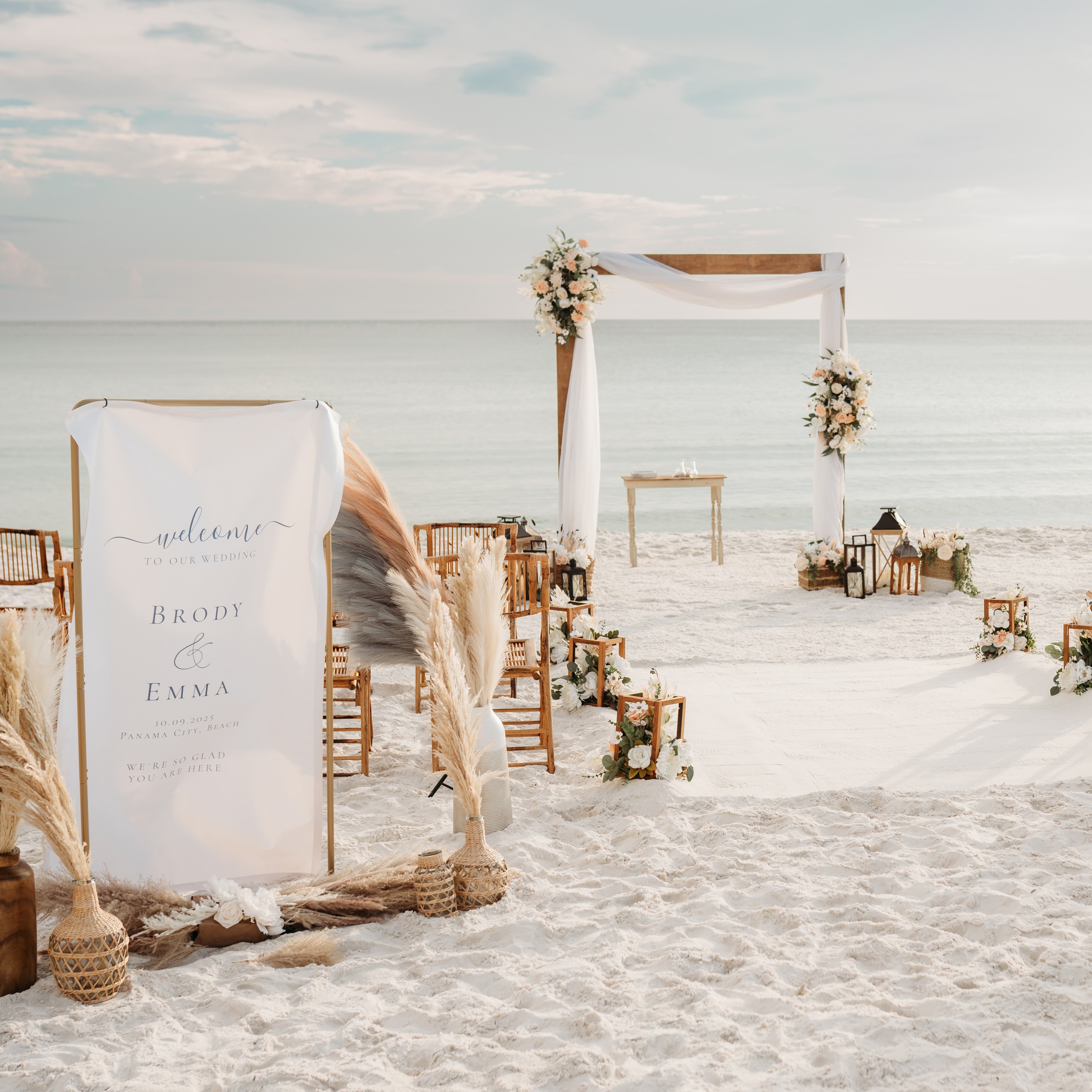 Beach wedding setup with arch, chairs, and decorative elements on a sandy beach.