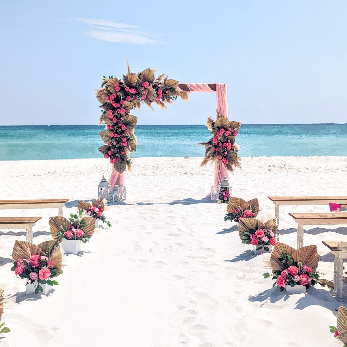 Beach wedding setup with floral arch and decorations on a sandy beach.