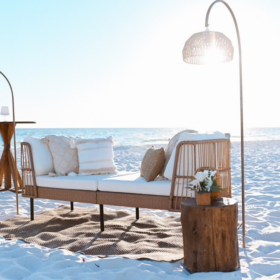 Wicker outdoor sofa with cushions on a sandy beach with ocean view