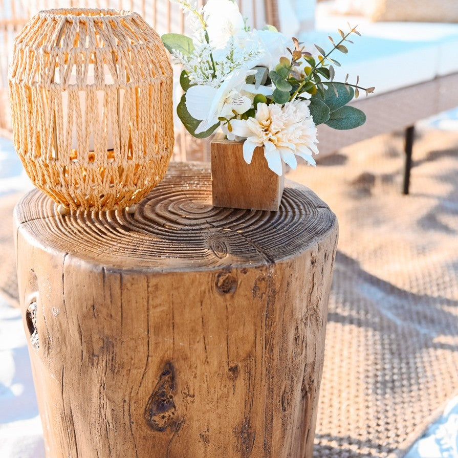 Wooden log table with a woven lantern and floral arrangement on a blurred beach background