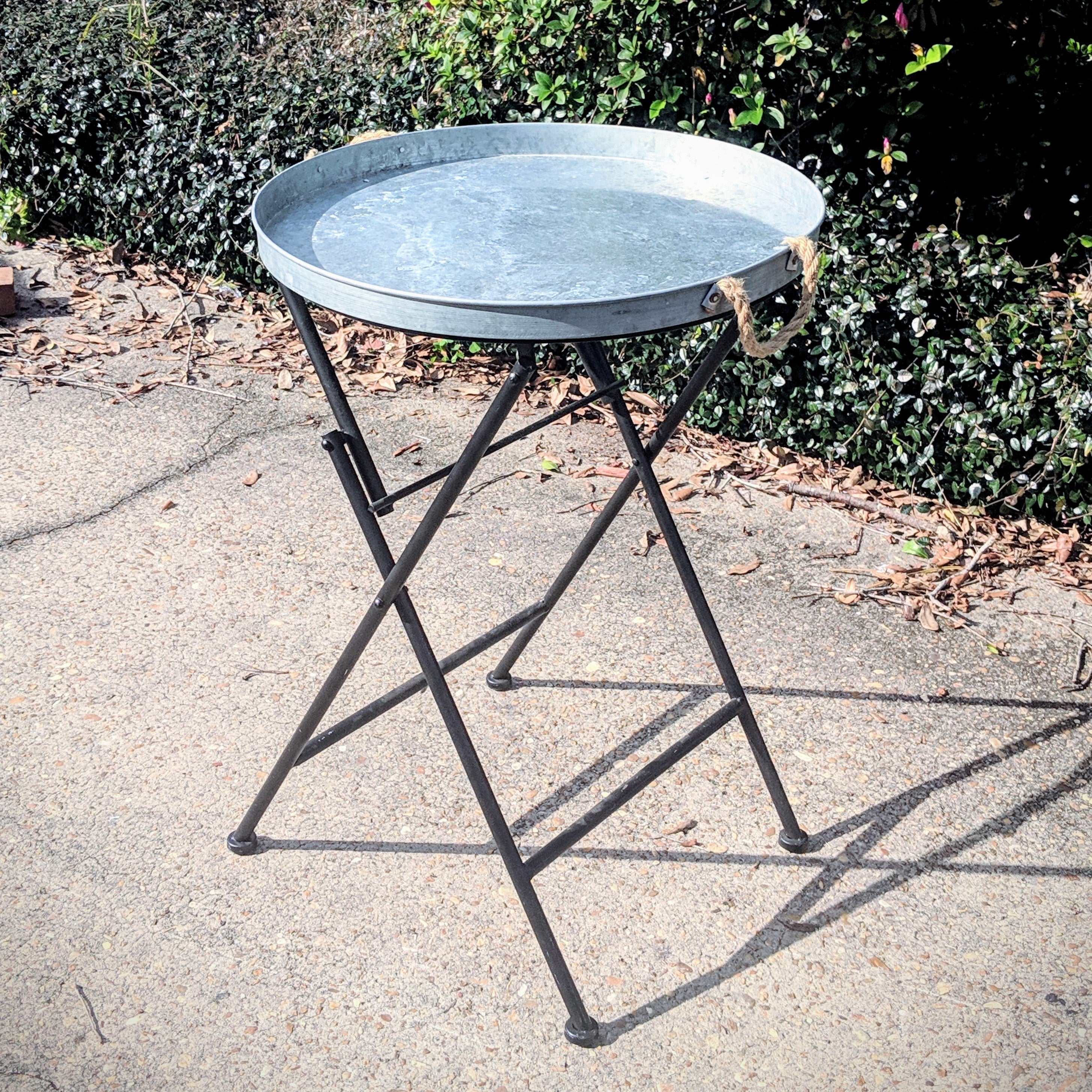 Small metal table on a stand outdoors with greenery in the background