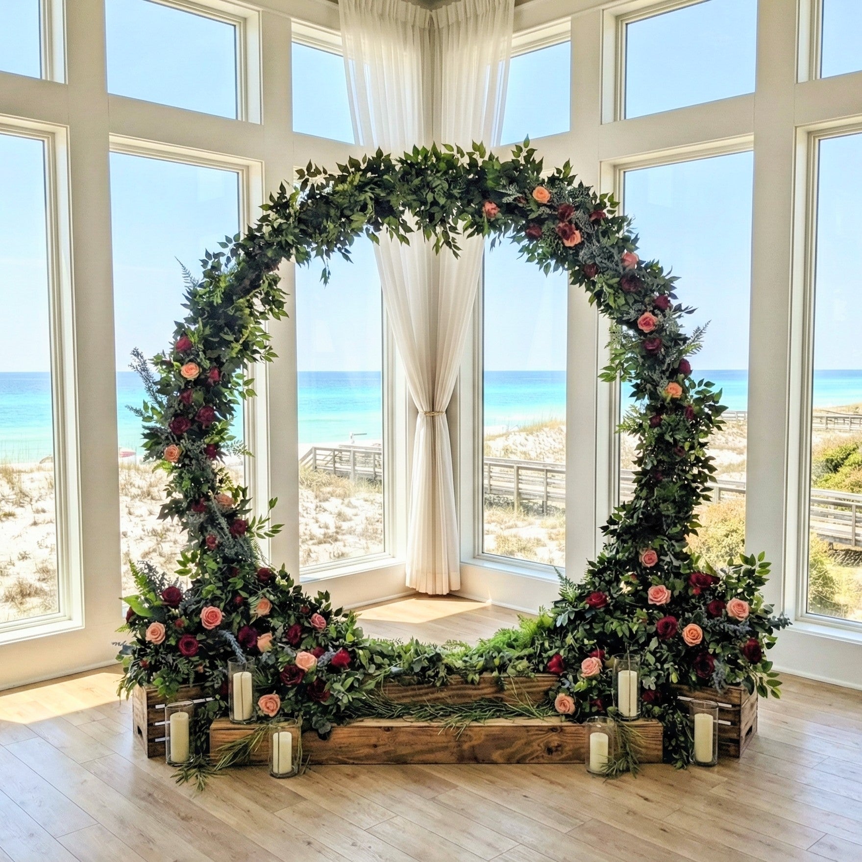 Decorative floral wedding arch rental with candles in a room with large windows overlooking a beach in 30A