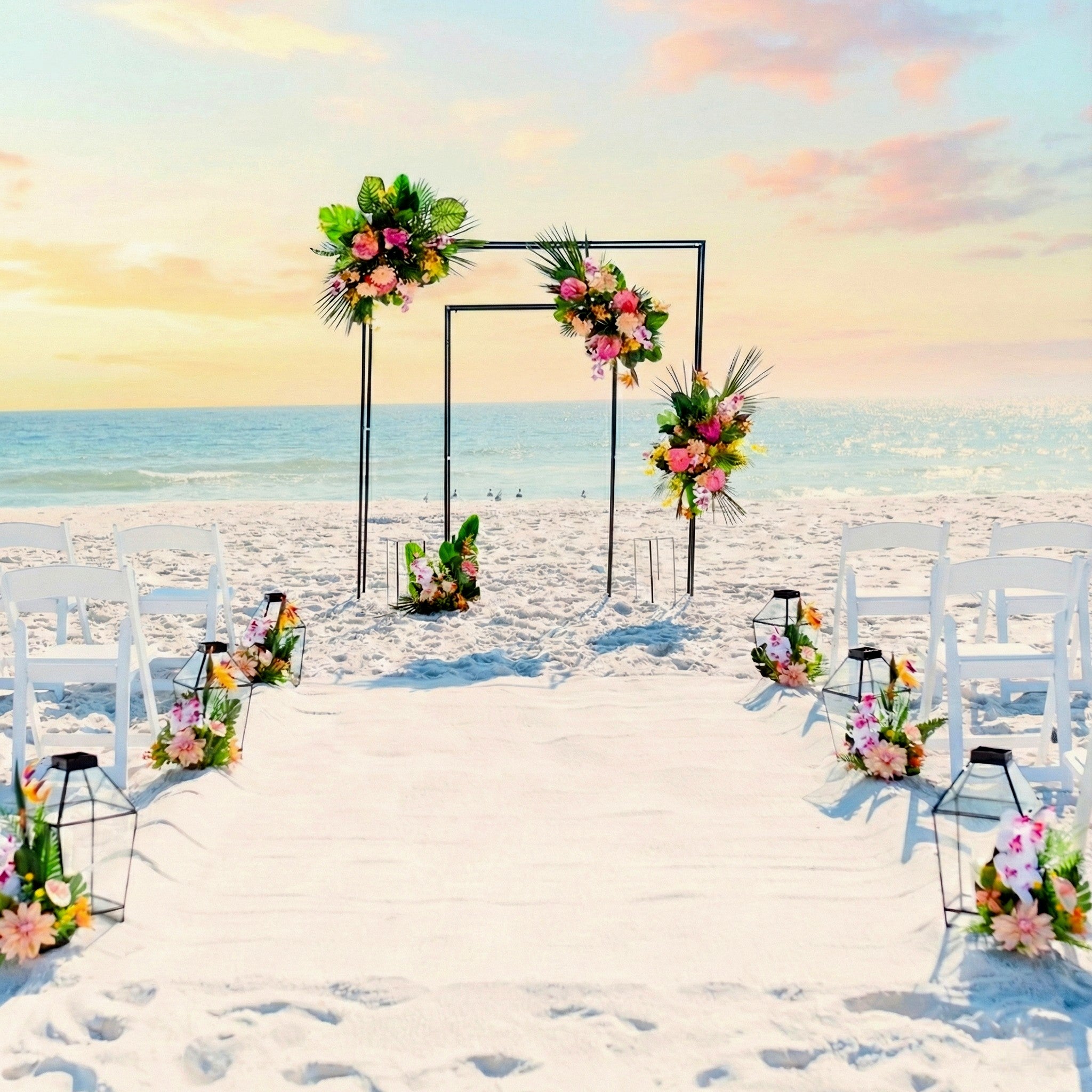 Beach wedding setup with floral arches and chairs under a sunset sky.