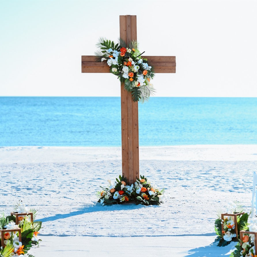 Wooden wedding cross with floral arrangements on a sandy beach with ocean in the background