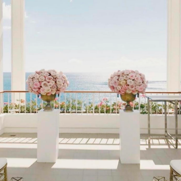 Two large floral arrangements on a white table with a scenic ocean view in the background.