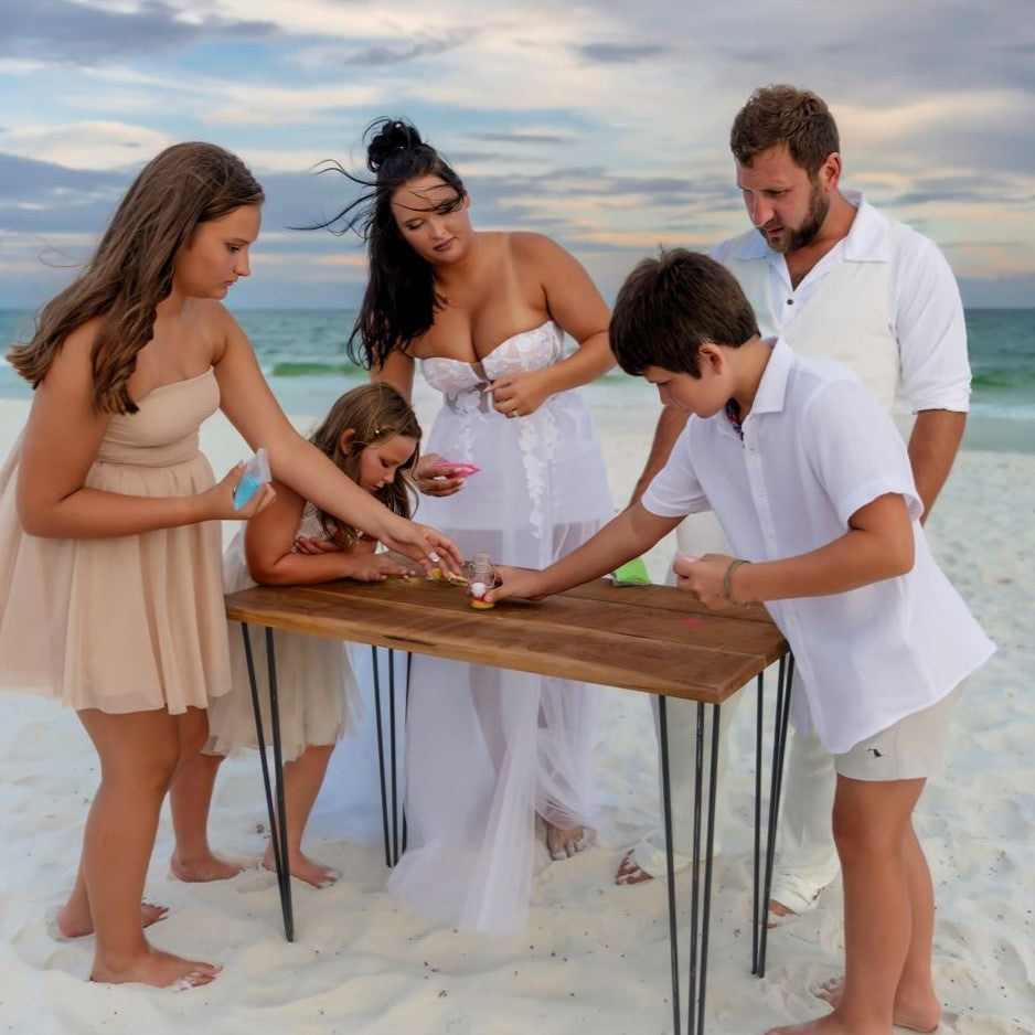 Family of five gathered around a wooden table on a sandy beach.