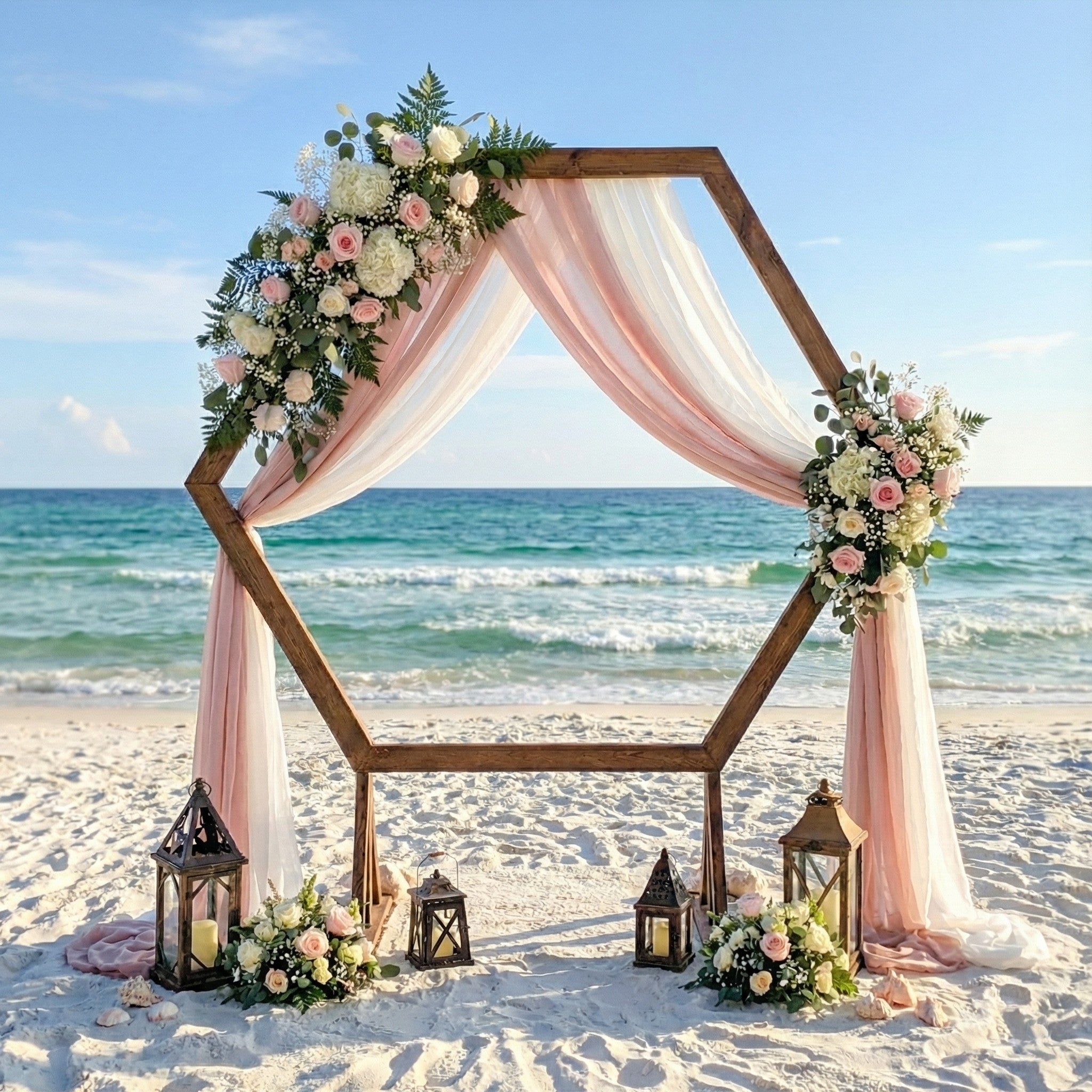 Hexagonal wedding arch on a beach with floral decorations and lanterns.