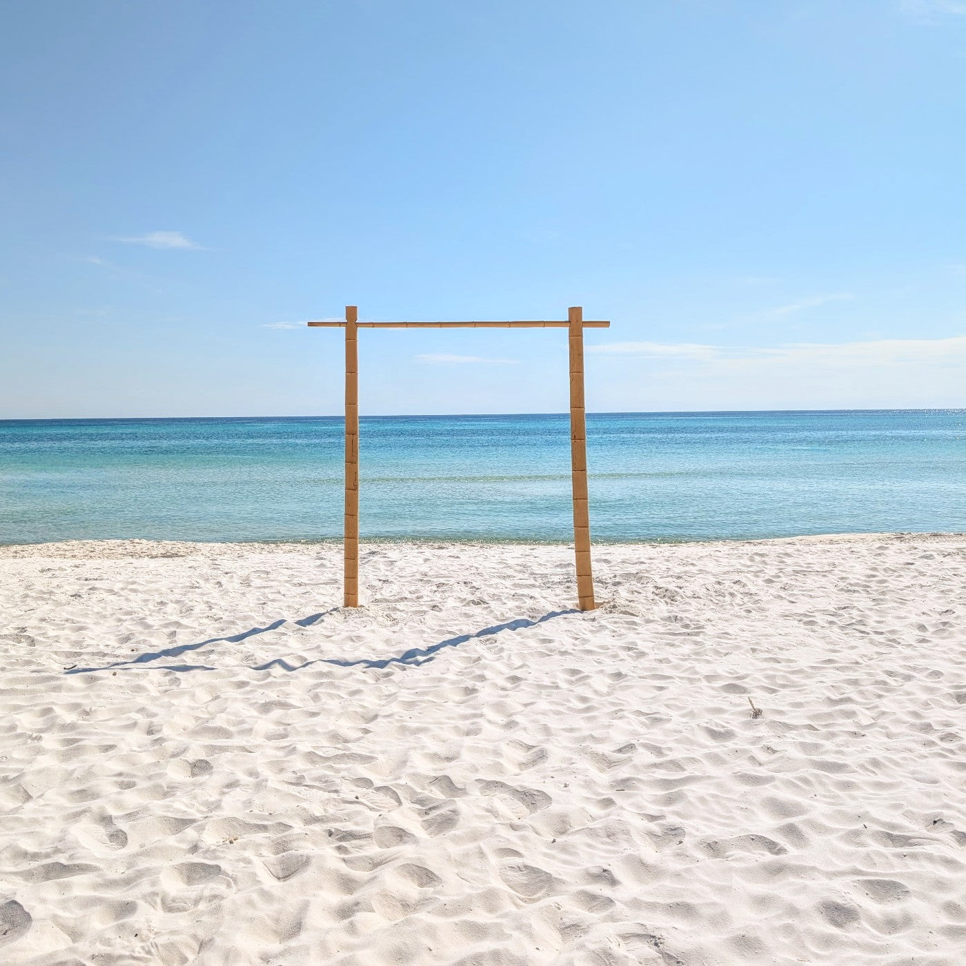Bamboo wedding arch rental in Panama City beach on the sandy beach with clear blue sky and ocean.