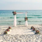 Beach wedding setup with floral arch and decorations in front of the ocean.