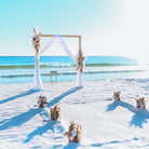 Beach wedding setup with arch and chairs on a sandy beach.