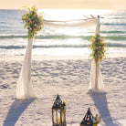 Beach wedding setup with wildflower accents and lanterns on a sandy beach.