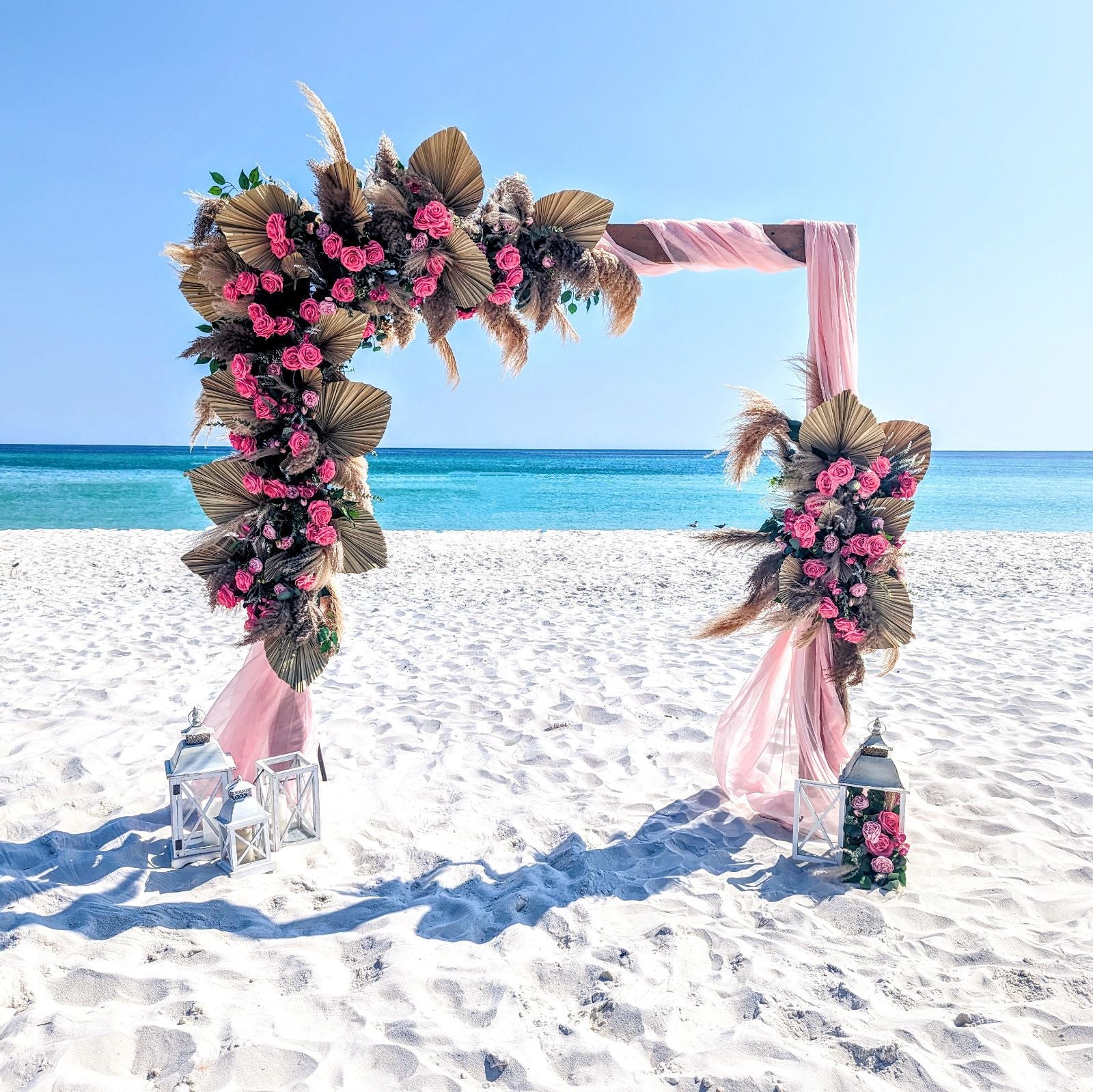 Decorative arch with flowers and pink fabric on a sandy beach with ocean view