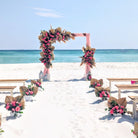 Beach wedding setup with floral arch and decorations on a sandy beach.