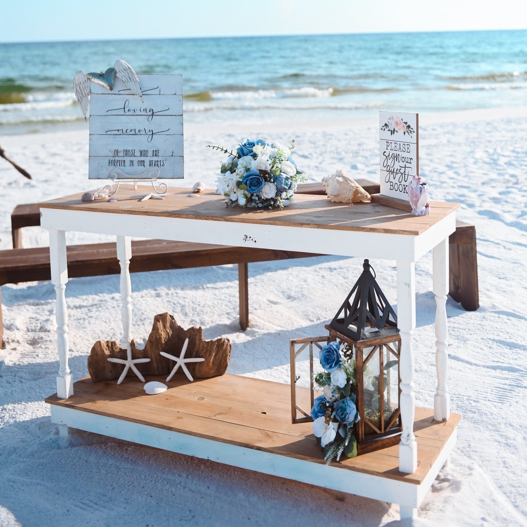 Decorative welcome table rental with flowers and lanterns on a sandy beach with ocean view