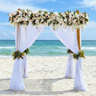 Decorative arch with flowers and white curtains on a beach with ocean view