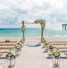 Beach wedding setup with floral arches and tables under a blue sky.