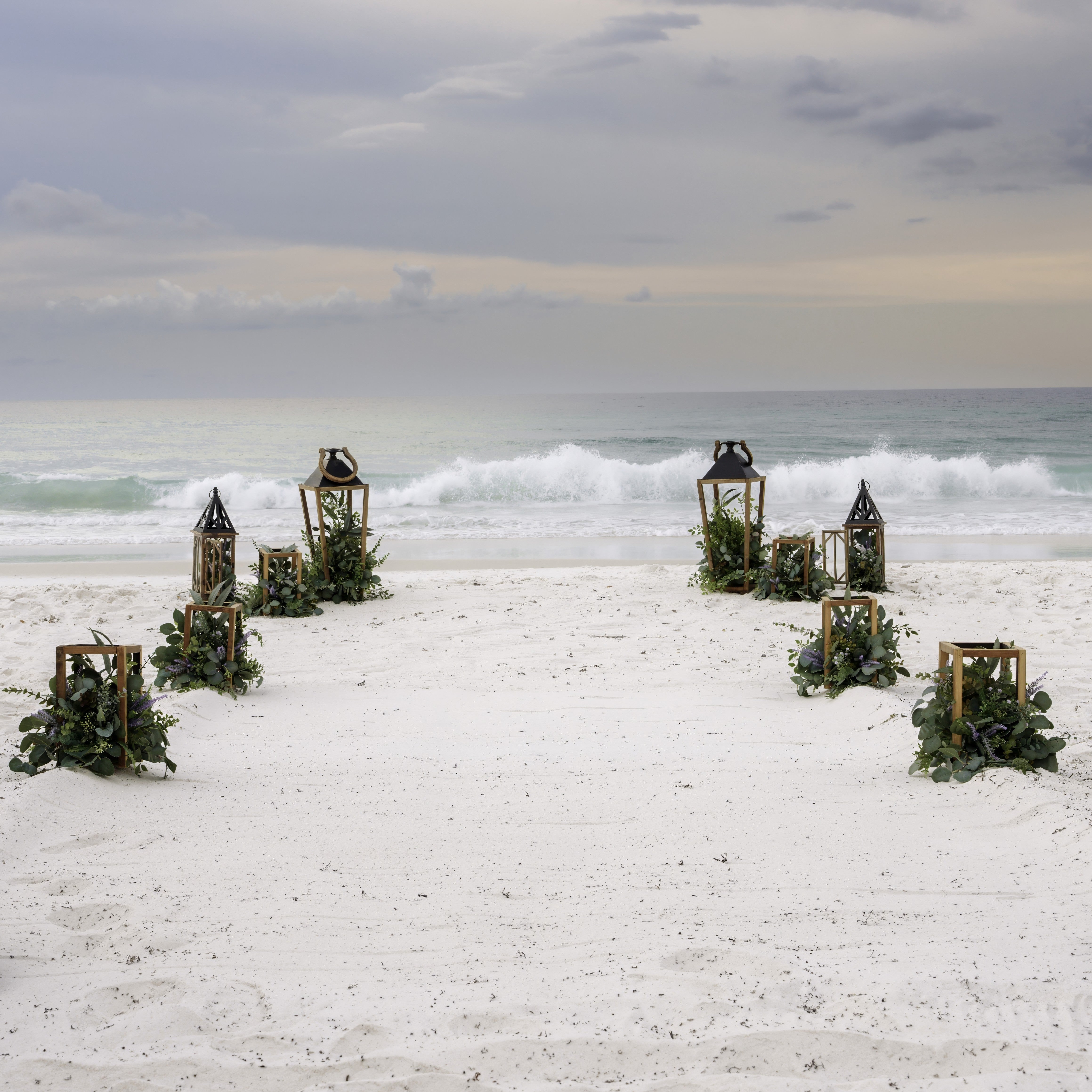 Decorative lanterns with greenery on a sandy beach with ocean waves in the background