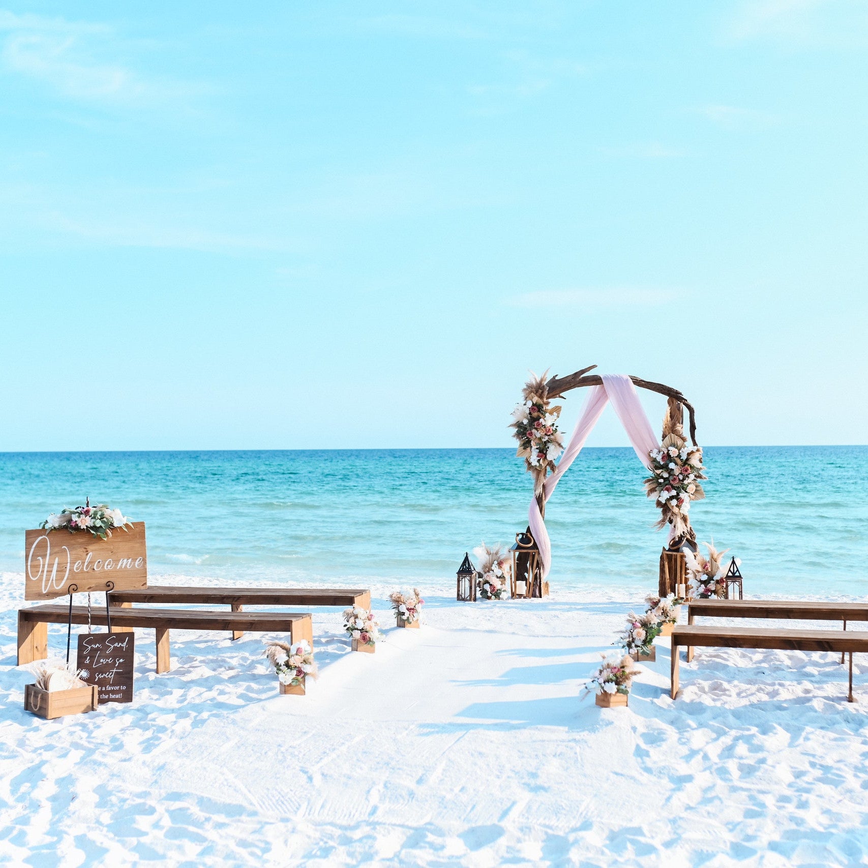 Brown wood bench rentals for destination beach weddings in Panama City Beach Florida with wood welcome sign, fan favor station for guests, driftwood wedding arbor arch, wood flower box aisle markers, and custom artificial flower rentals from The Wedding Shop in Panama City Beach.