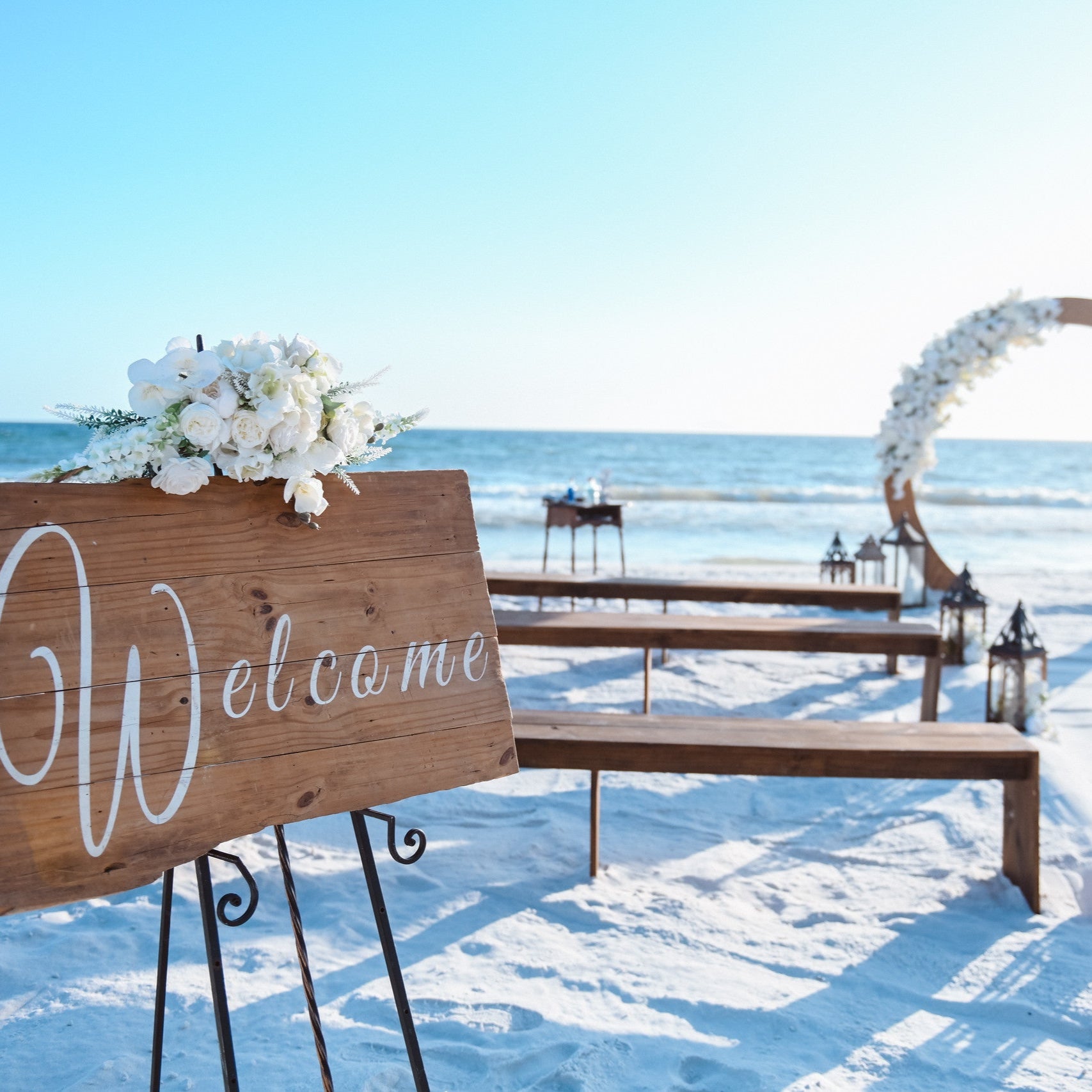 Brown wood bench rentals with matching wood welcome sign and wood circle moon gate arbor in PCB Panama City Beach Florida