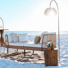 Wicker outdoor sofa with cushions on a sandy beach with ocean view