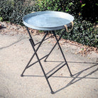 Small metal table on a stand outdoors with greenery in the background