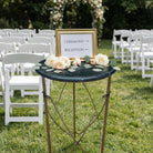 Decorative table rental with flowers and a sign indicating ceremony and reception areas at an outdoor wedding venue.