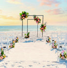 Beach wedding setup with floral arches and chairs under a sunset sky.