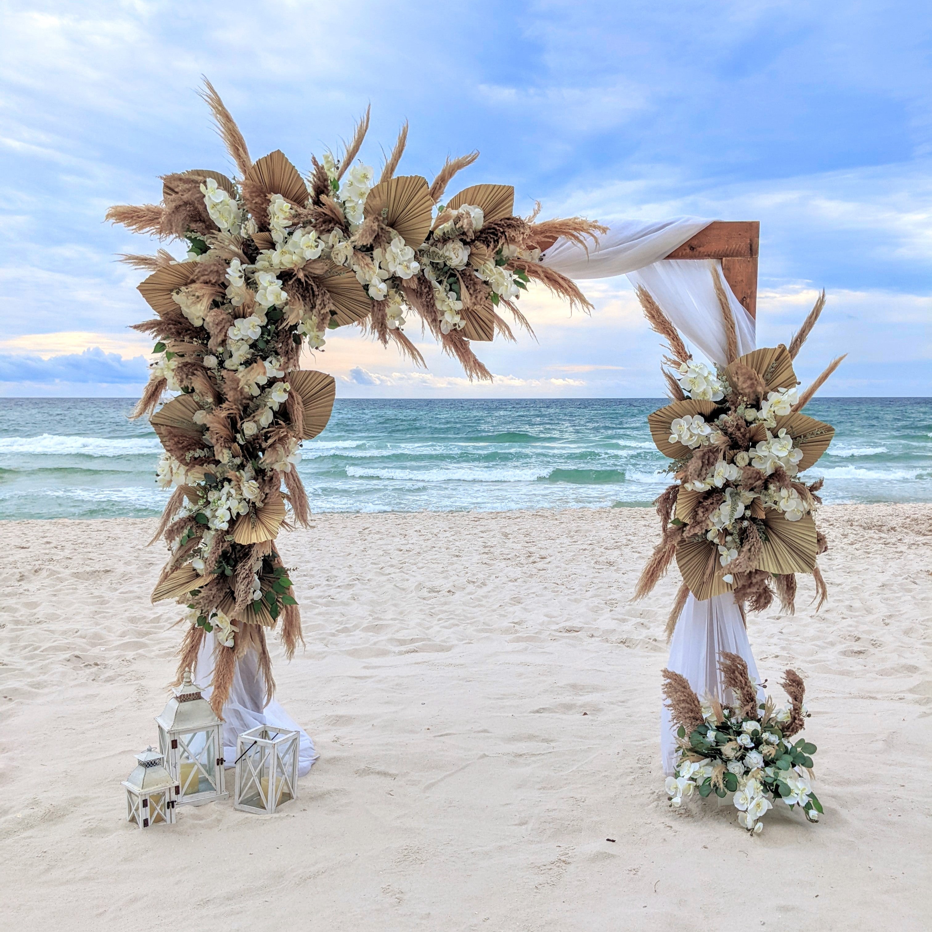 Decorative wedding arch rental with flowers and pampas grass on a sandy beach with ocean view in panama city beach