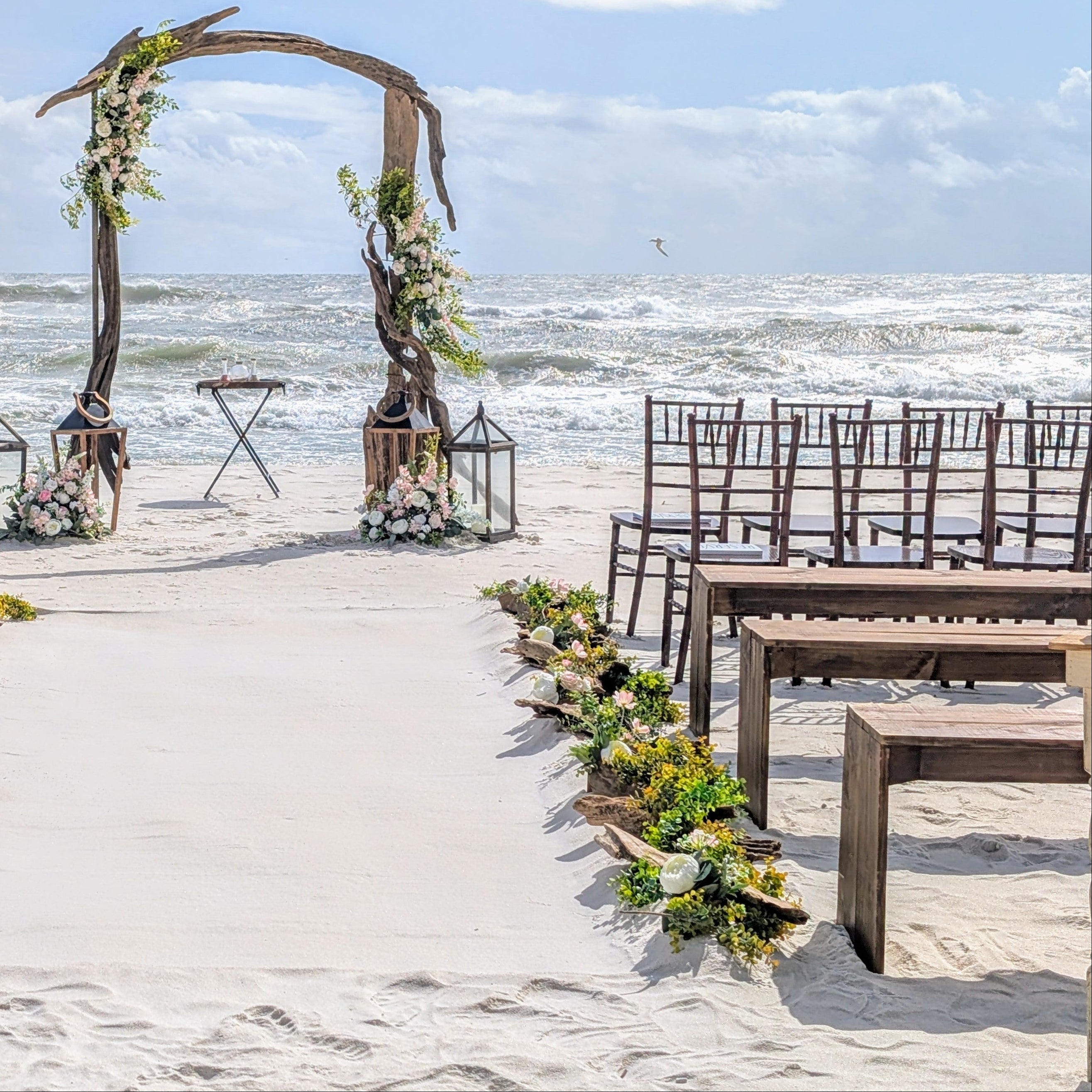 mahogany chiavari chair rental in PCB at a beach wedding used for honored guest seating on first 2 rows at the ceremony with driftwood arbor, driftwood aisle markers, and rough gulf waves