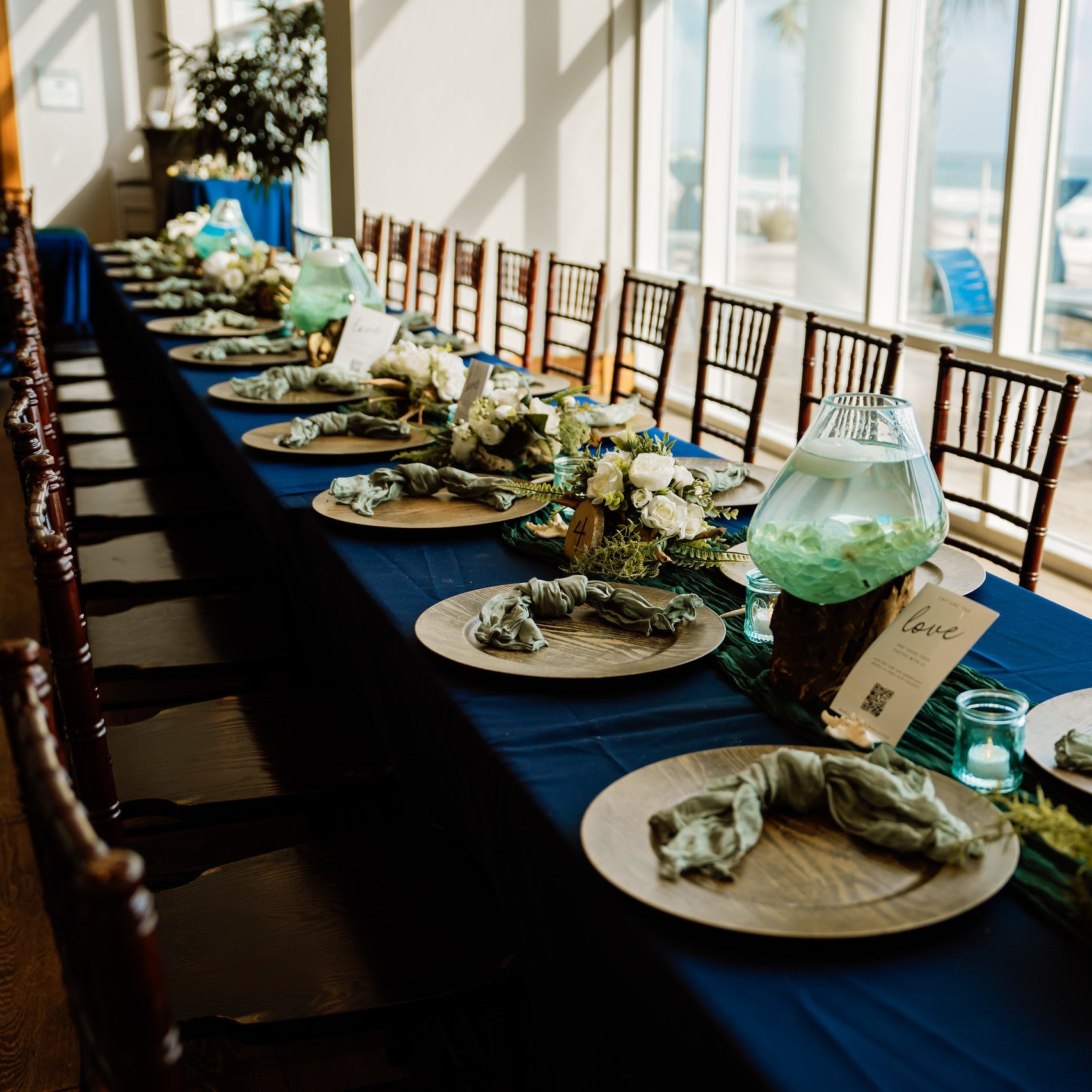 Mahogany chiavari chair rentals in panama city beach for a wedding reception with navy linens on the table with wood charger plates, knotted napkins, and driftwood and flower centerpieces by The Wedding Shop