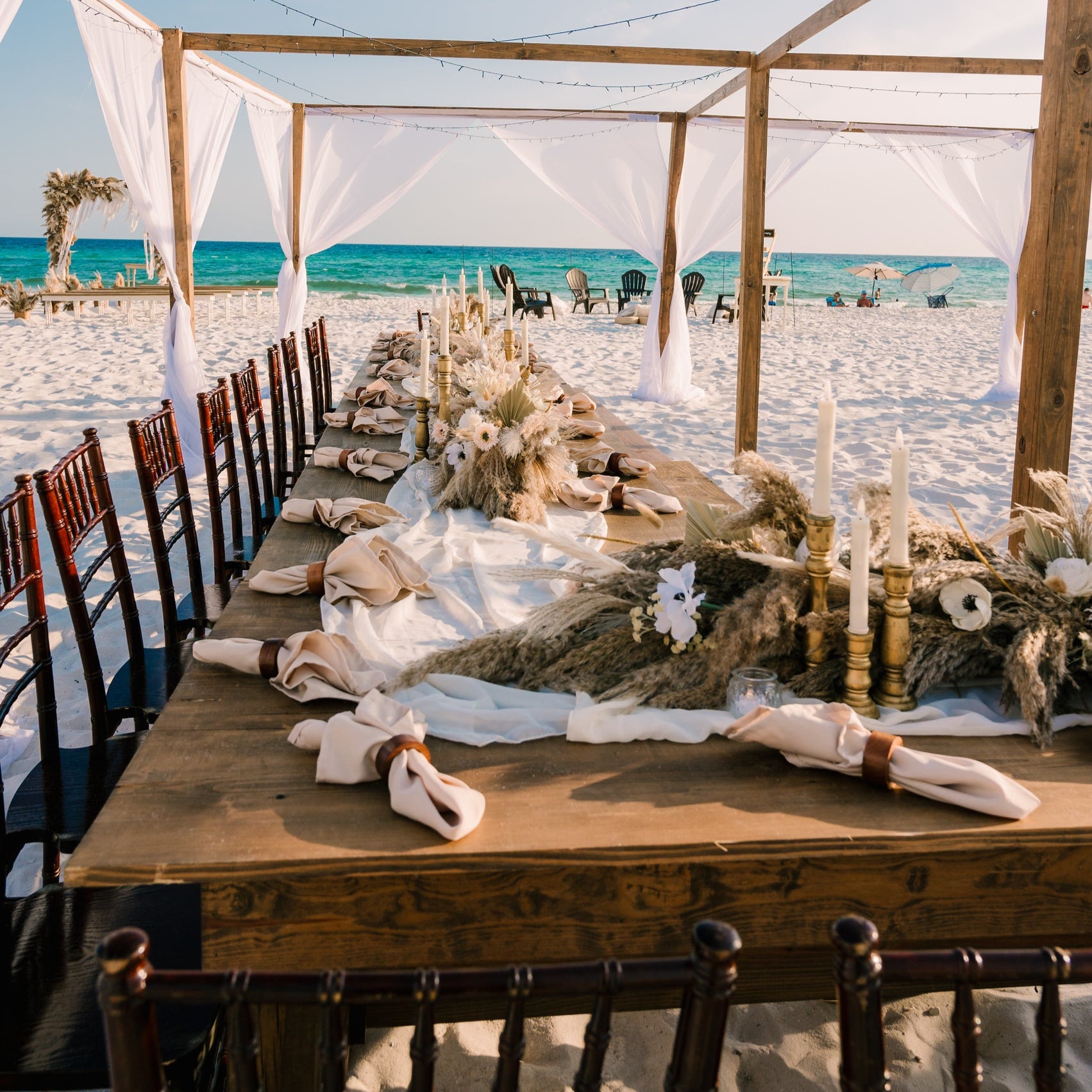 Mahogany chiavari chair rentals in panama city beach used with farmhouse tables for a lux beach wedding reception in PCB with boho pampas grass centerpieces and our exclusive open air tent