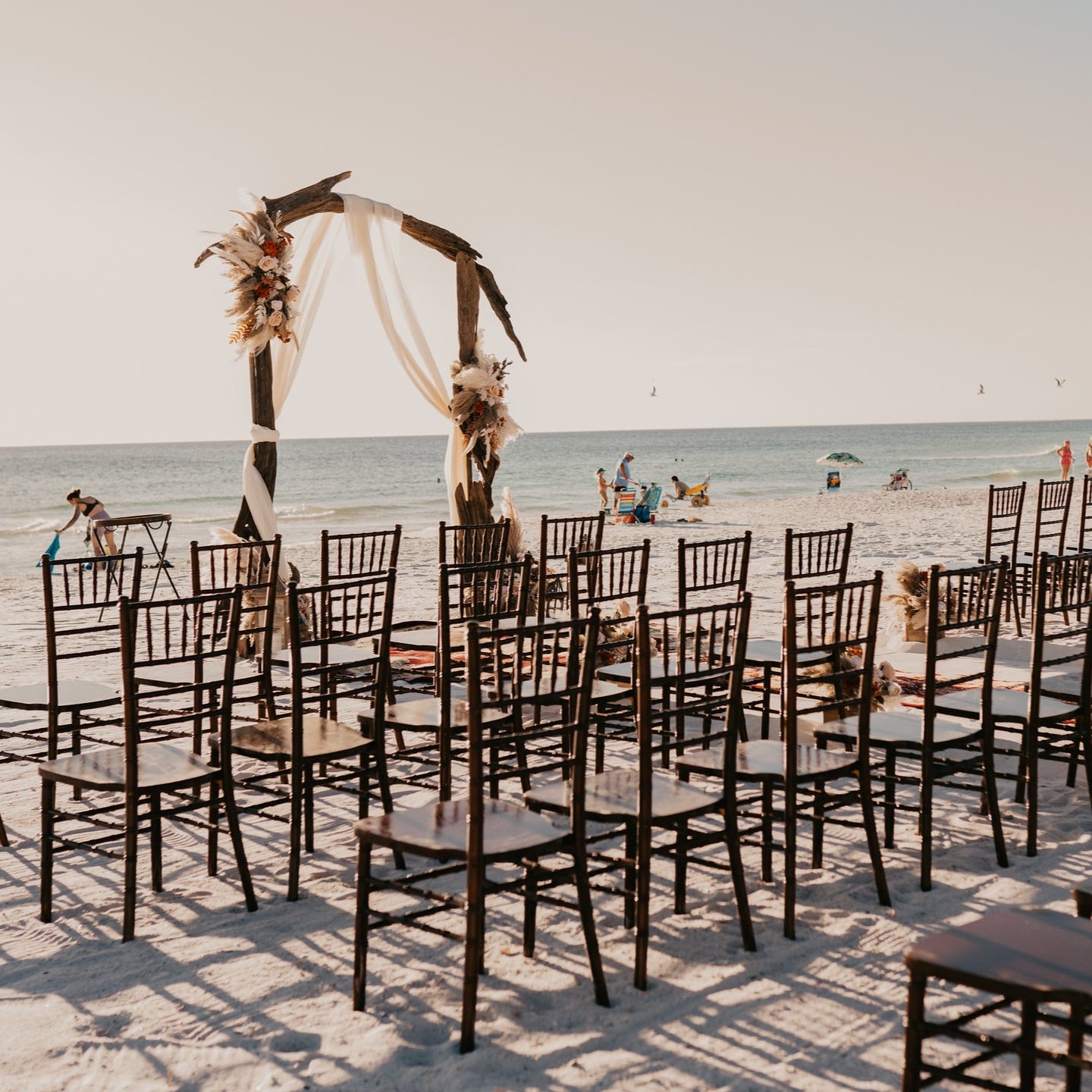 Beach wedding ceremony decoration setup with driftwood arbor and mahogany chiavari chair rentals in panama city beach with wedding flowers by The Wedding Shop