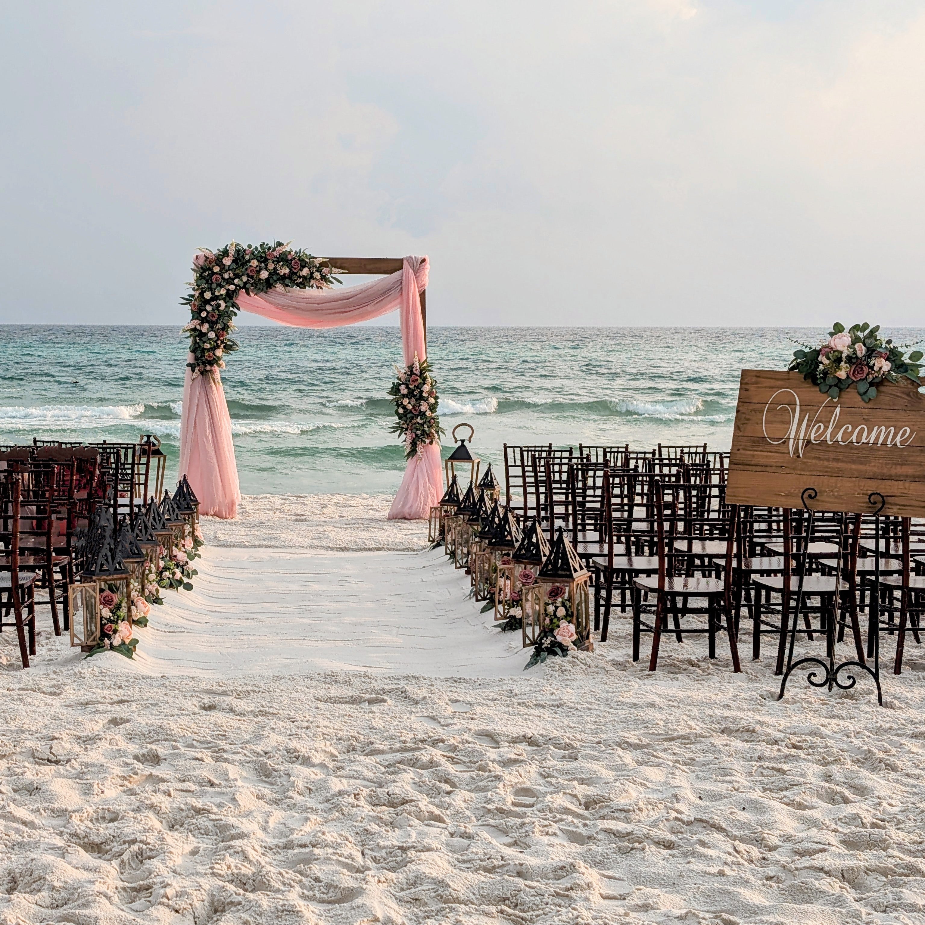 Mahogany chiavari chair seating for a beach wedding in panama city beach florida with a wood wedding welcome sign and custom artifical flower rentals from The Wedding Shop