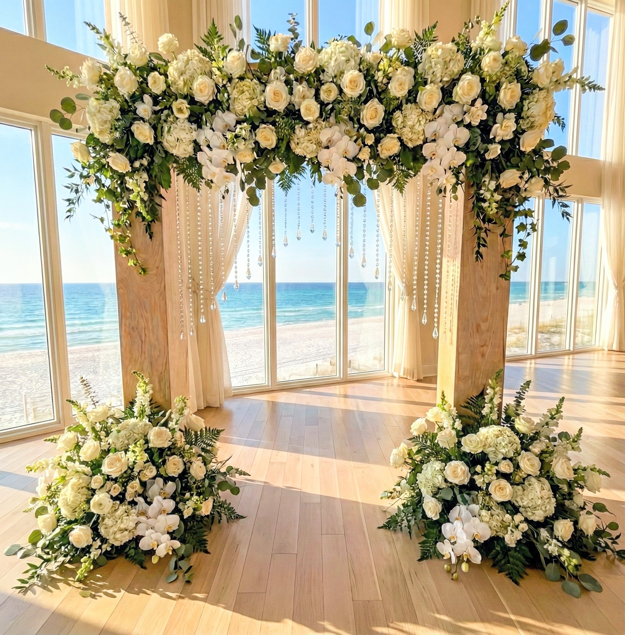 Floral arch and decorations in a room with large windows overlooking a beach.