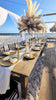 Brown wood bench rentals in Panama City Beach paired with our farmhouse tables for a lux beach reception under our open air tent in PCB with big boho pampas grass centerpieces rented from The Wedding Shop.