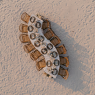 Aerial view of a wedding setup with chairs and serpentine tables on sand.