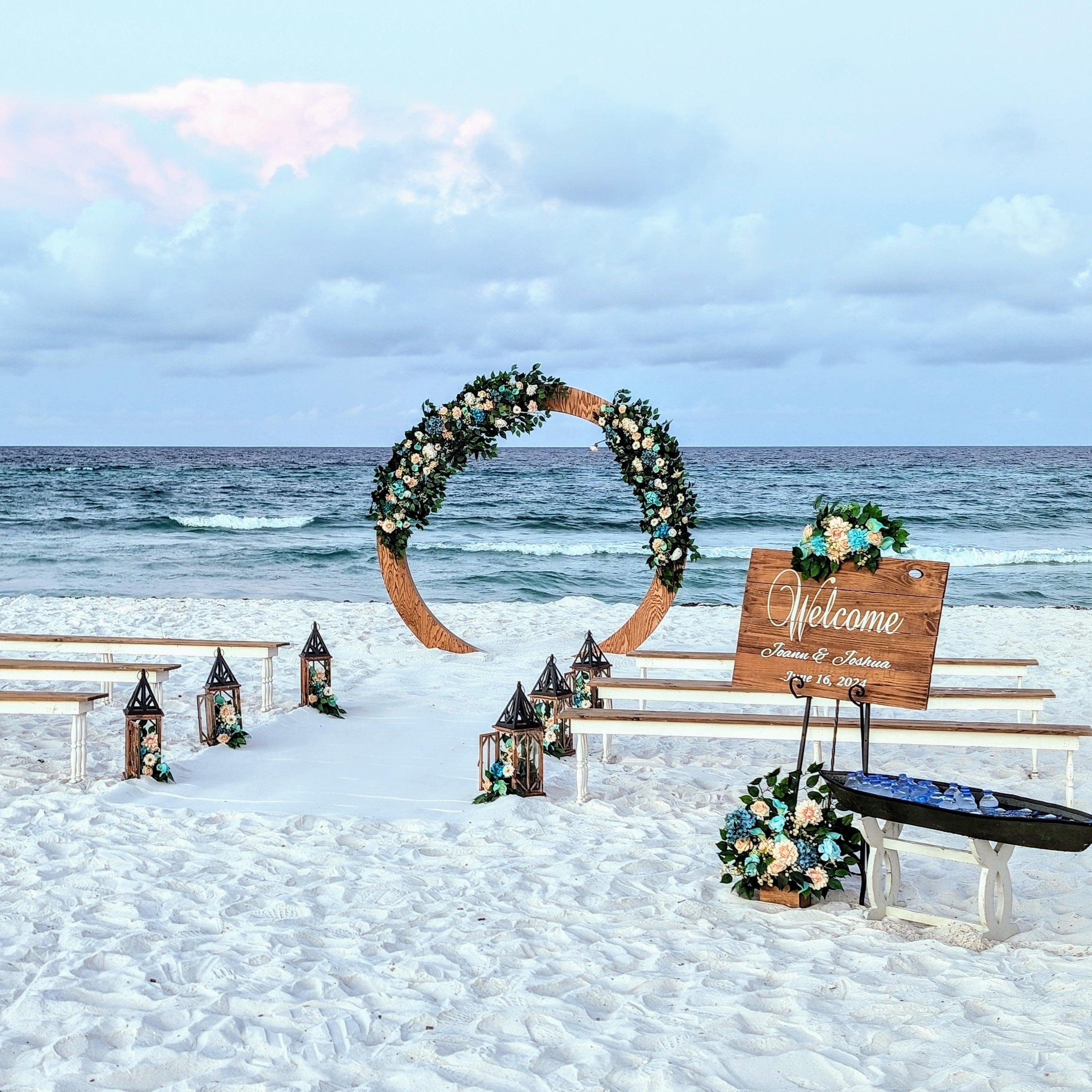 2-toned spindle leg bench seating rental for a beach wedding ceremony with wood circle moon gate arbor lantern clusters and romantic peach and blue flowers by the weddings shop for a beach wedding in panama city beach on the emerald coast