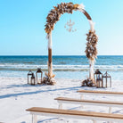 2-toned spindle leg bench seating rental for a beach wedding ceremony with dome arbor lantern clusters and beachy boho flowers by the weddings shop for a beach wedding in panama city beach on the emerald coast