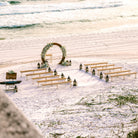 2-toned spindle leg bench seating rental for a beach wedding ceremony with wood circle wedding arbor lantern clusters and classic white flowers by the weddings shop for a beach wedding in panama city beach on the emerald coast