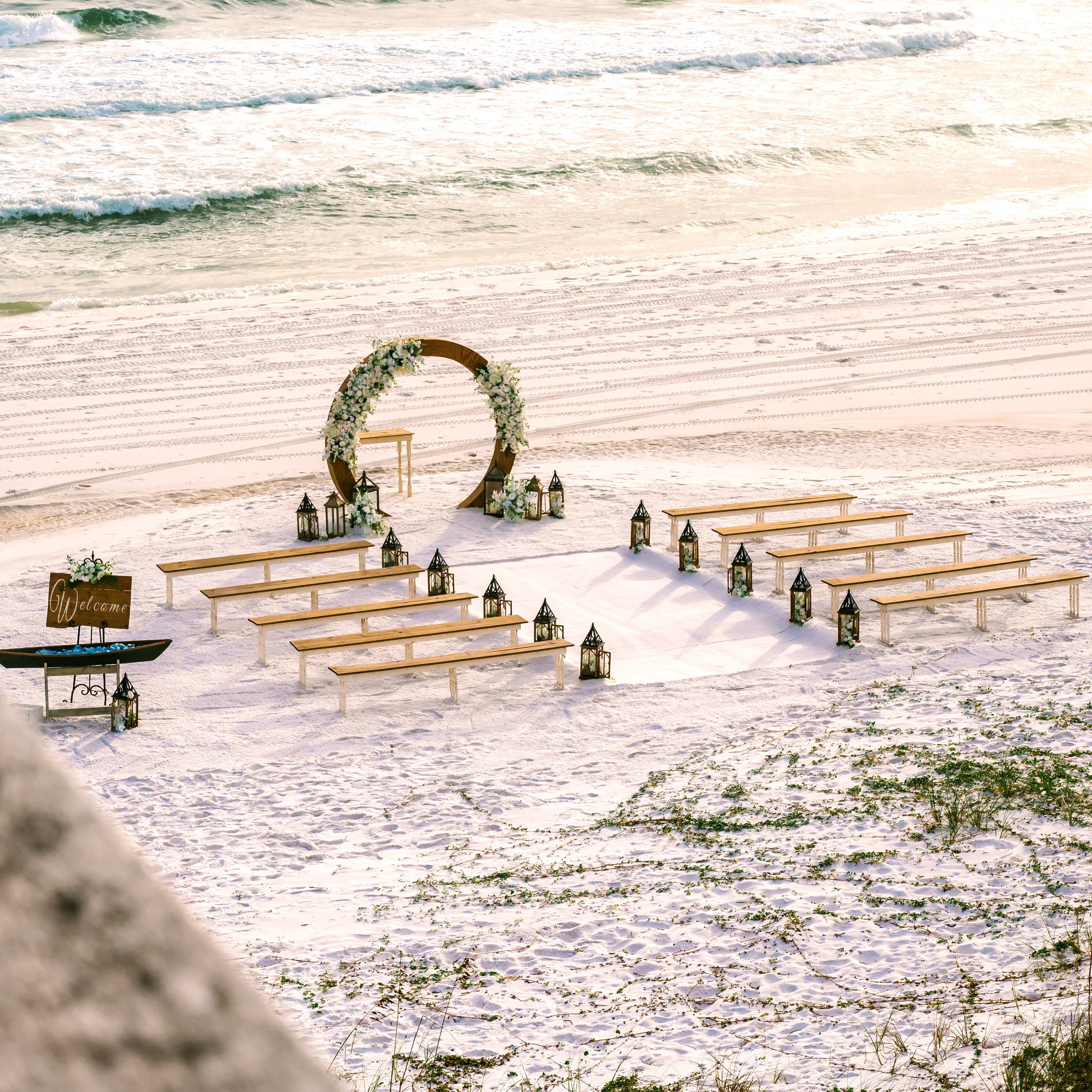 2-toned spindle leg bench seating rental for a beach wedding ceremony with wood circle wedding arbor lantern clusters and classic white flowers by the weddings shop for a beach wedding in panama city beach on the emerald coast