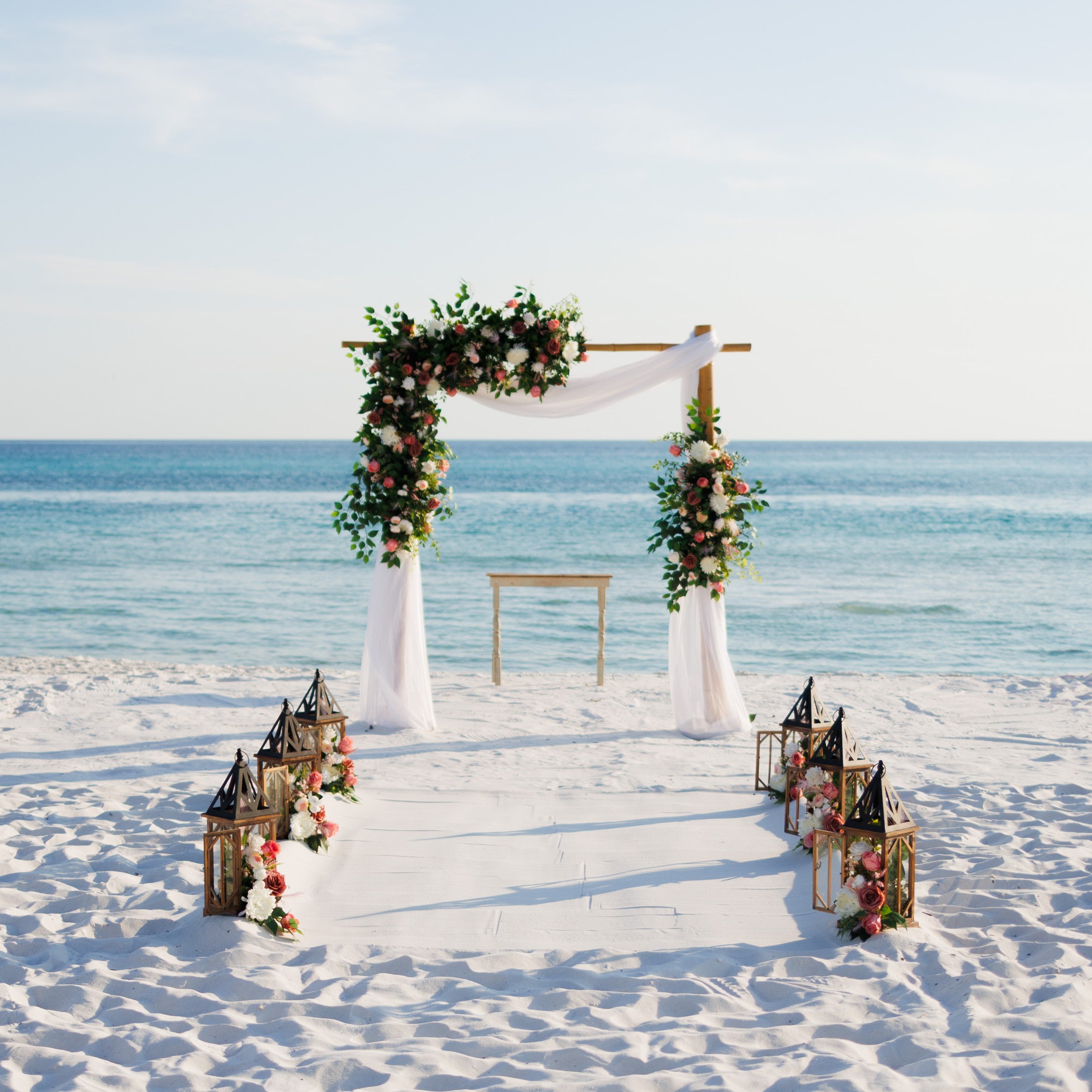 Decorative arch with flowers and lanterns on a sandy beach with ocean view