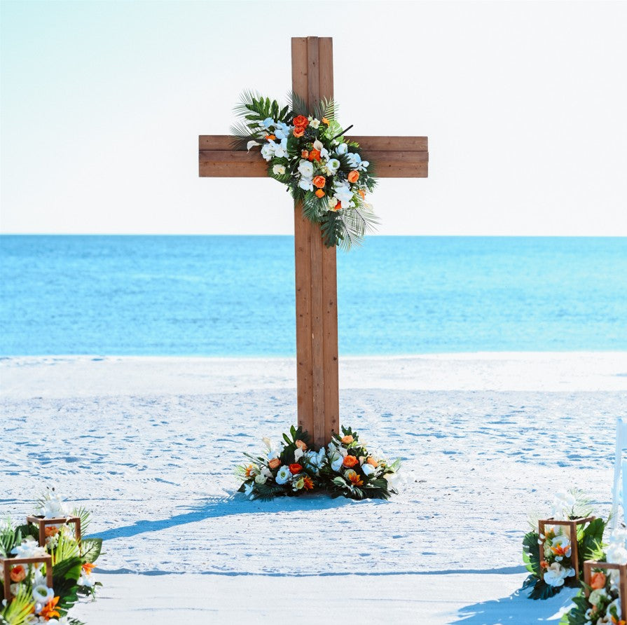 Wooden wedding cross with floral arrangements on a sandy beach with ocean in the background