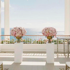 Two large floral arrangements on a white table with a scenic ocean view in the background.
