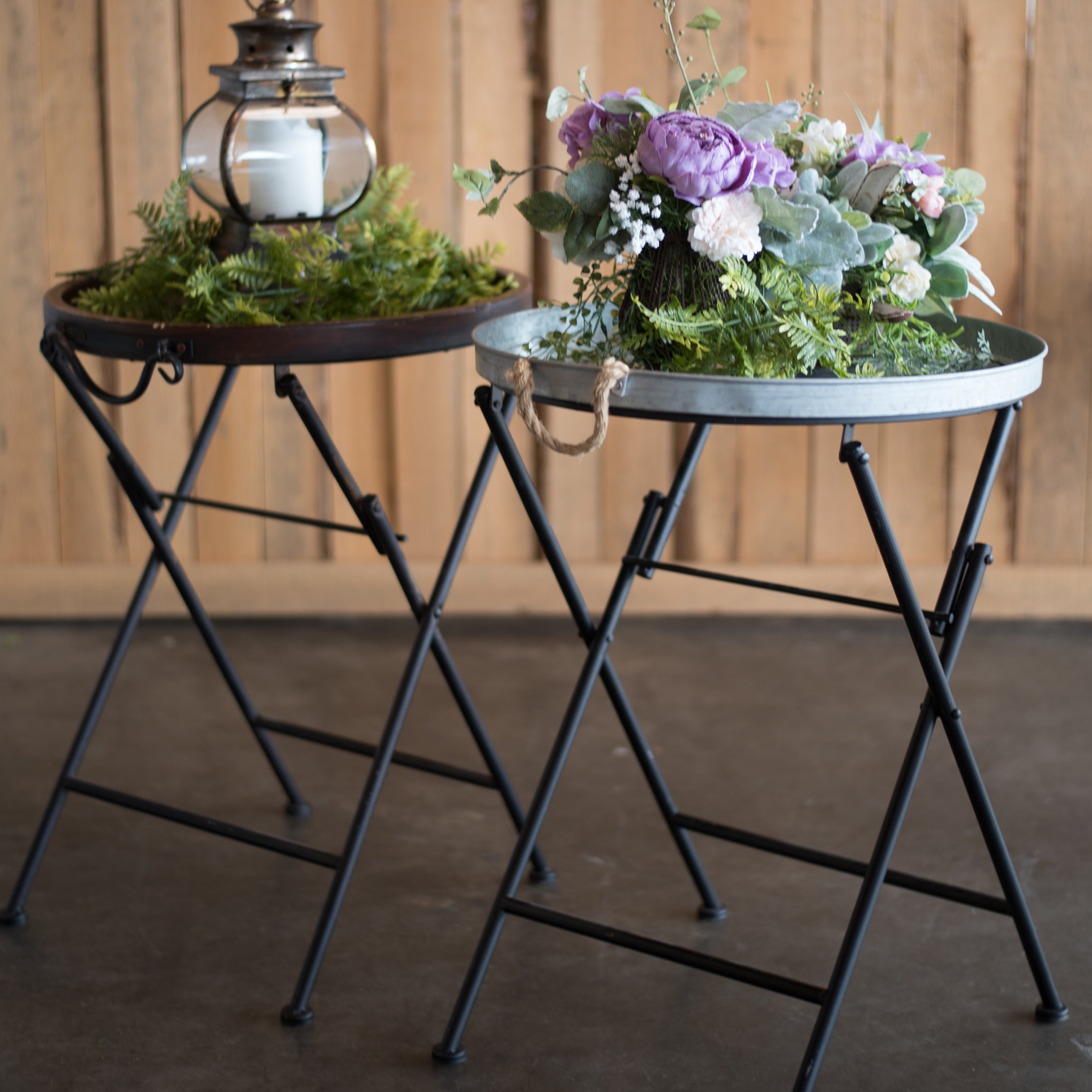 Two small black metal tables with decorative items against a wooden paneled wall.