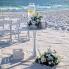 white pedestal table rental with beverage station on the beach for a beach wedding with white flowers. 