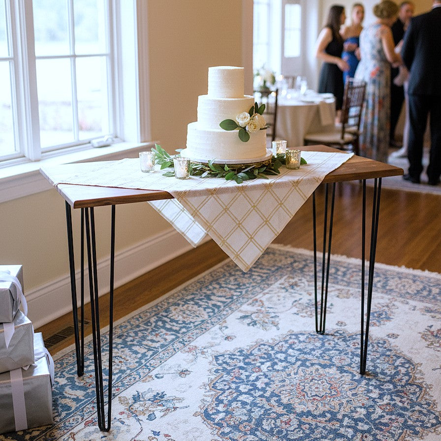 Three-tiered wedding cake on a walnut top table rental with people in the background 