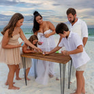 Family of five gathered around a wooden table on a sandy beach.